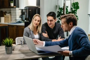 Young couple and real estate agent using laptop while going through housing plan on a meeting.